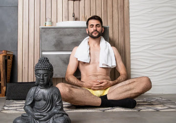 Lifestyle photo of a man meditating indoors while wearing yellow briefs and a towel around his shoulders